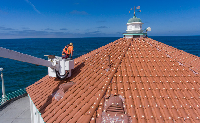 Learn the ins and outs of lift safety before taking on a big job like this, installing bird repellent dishes on the roof tiles of a pier structure. PHOTO: BIRD BARRIER