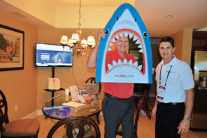 Chip Hughes, right, co-owns LabelSDS.com with his wife, Debbie. The pair went all in on branding their meeting room suite with a “Be a Business Shark” theme, replete with Debbie’s delicious “shark bait” snack mix, shark beverage cozies and the sharkhead cutout that the game Jerry Smith, Dial Pest Control, is pictured using. PHOTO: PMP STAFF